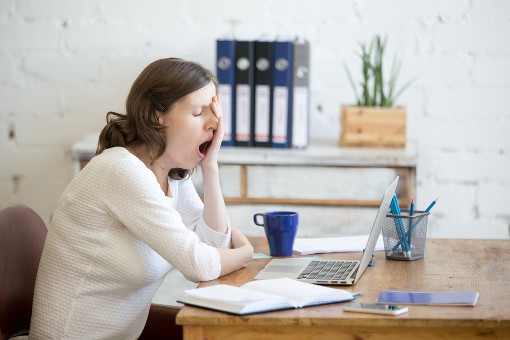 woman yawning at computer desk because she needs to learn how to increase energy levels
