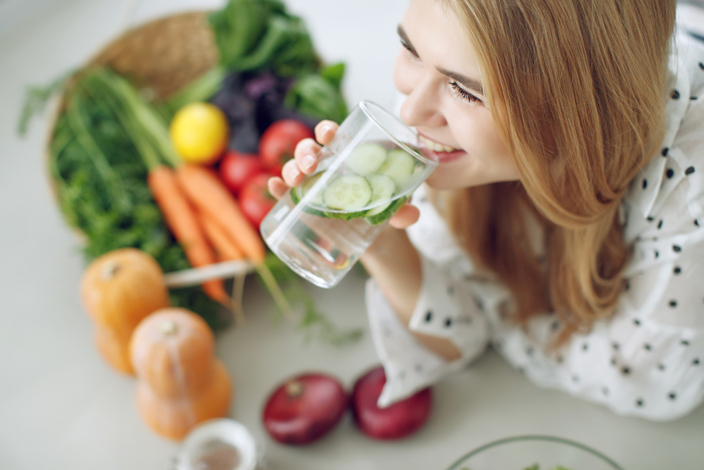 woman drinking cucumber water while prepping vegetables